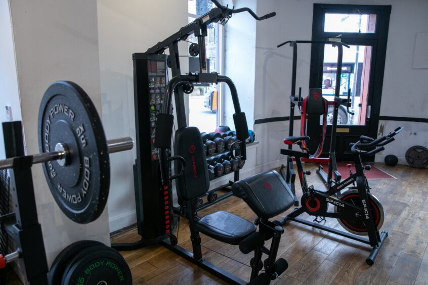 Gym interior with equipment lines up in front of large bright windows.