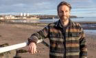 Image shows: Scott 'Mitch' Mitchell standing on the promenade in his adopted home town of Kirckaldy. Scott is wearing a lumberjack-style shirt and smiling at the camera. He has a beard.