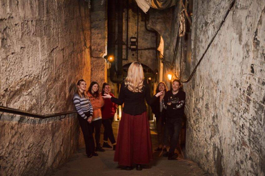 people listen to a guide in an alleyway that leads down underneath Edinburgh 