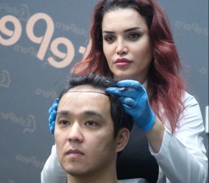 Man seated having scalp worked on by clinician.