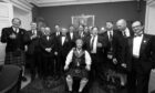 Black and white photo of group of men in kilts and formal wear at function