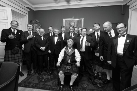 Black and white photo of group of men in kilts and formal wear at function