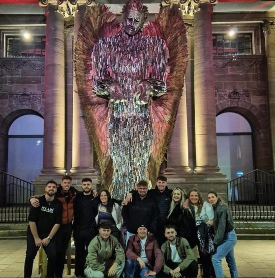 Group of people standing in front of Knife Angel statue lit up at night