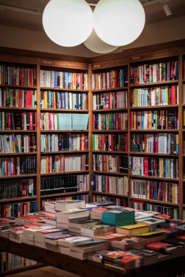 Image shows interior of Topping & Company Booksellers in St Andrews. A table in a corner with books stacked on the table and the bookshelves.