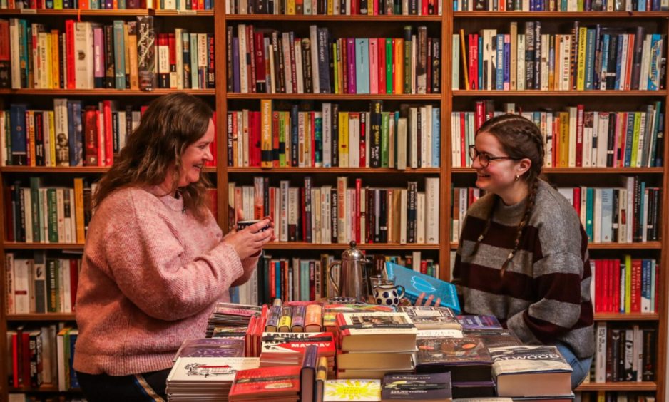 Image shows: feature writer Nora McElhone and bookseller Jen Thomas chatting over a coffee. They are sitting in a small room lines with books in Topping & Company, St Andrews.