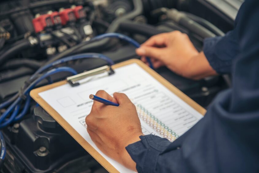 a mechanic looking at an engine holding a checklist