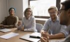 Diverse team of happy colleagues having fun at meeting table, talking, discussing team success, brainstorming on creative ideas, work tasks, planning strategy, laughing, enjoying cooperation