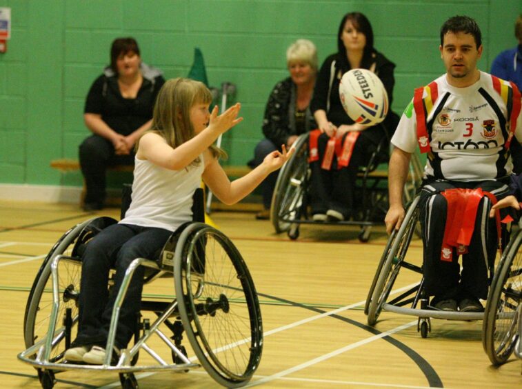 a young girl in a wheelchair passes a rugbyy ball during a game at the launch of the city's Wheelchair Rugby League Club.