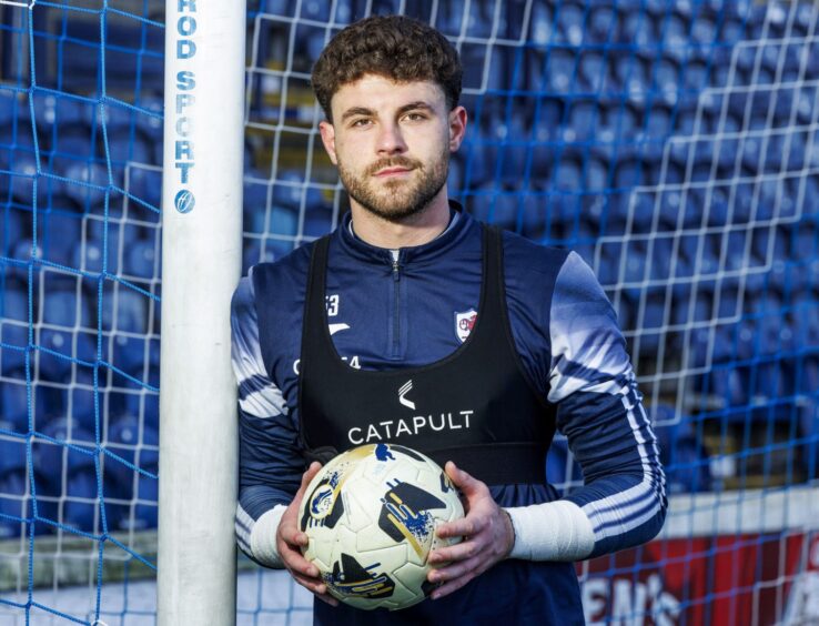 Josh Rae leans against a goalpost holding a football.