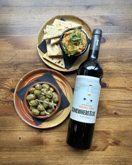 a bottle of wine on a table with a bowl of olives and a plate filled with slices of bread and some dip