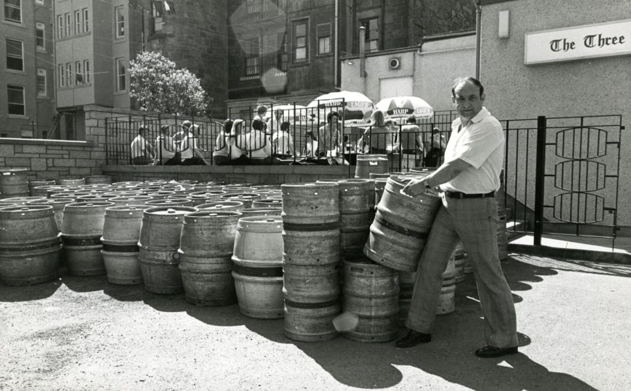 a man carries a beer keg to stack it beside some others as Sunday drinkers enjoying the sunshine on the patio.