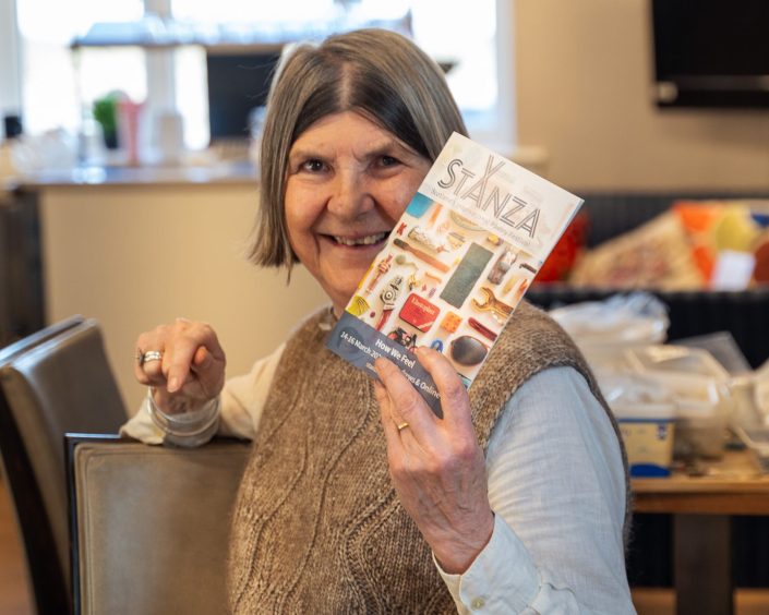 Image shows: a volunteer at the North East Fife Community Hub in St Andrews holding up a StAnza festival programme.