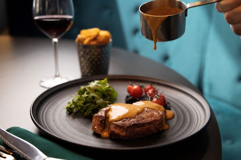 Steak sauce drips from a small metal pot on to steak.