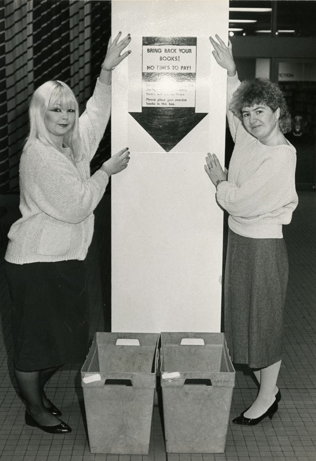 Library workers beside a poster advertising the amnesty on overdue books in January 1987.