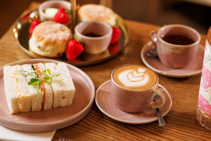 a close up of a table with an afternoon tea spread at Hatch in St Andrews. The selection includes finger sandwiches, scones, strawberries and a coffee.