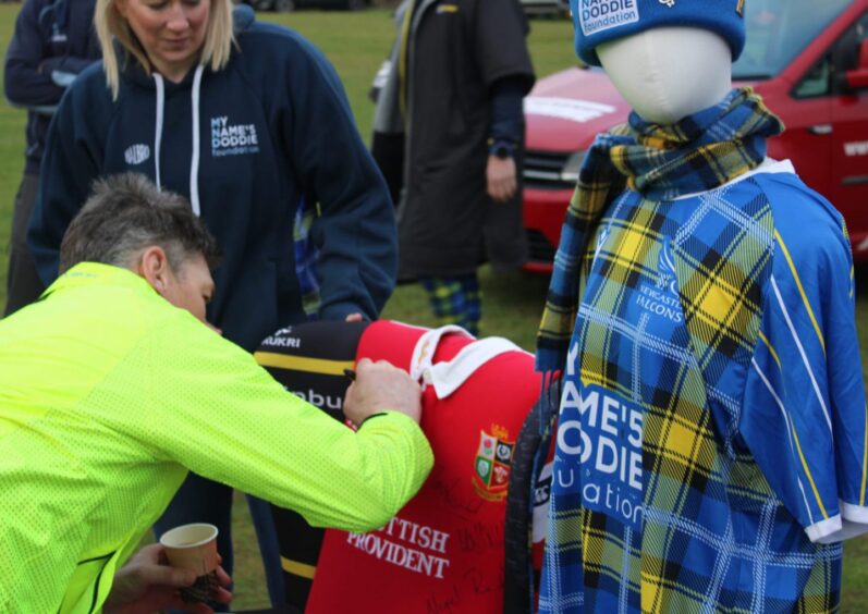 Rob Wainwright signing name on chair made from rugby shirts while Jayne Strachan looks on