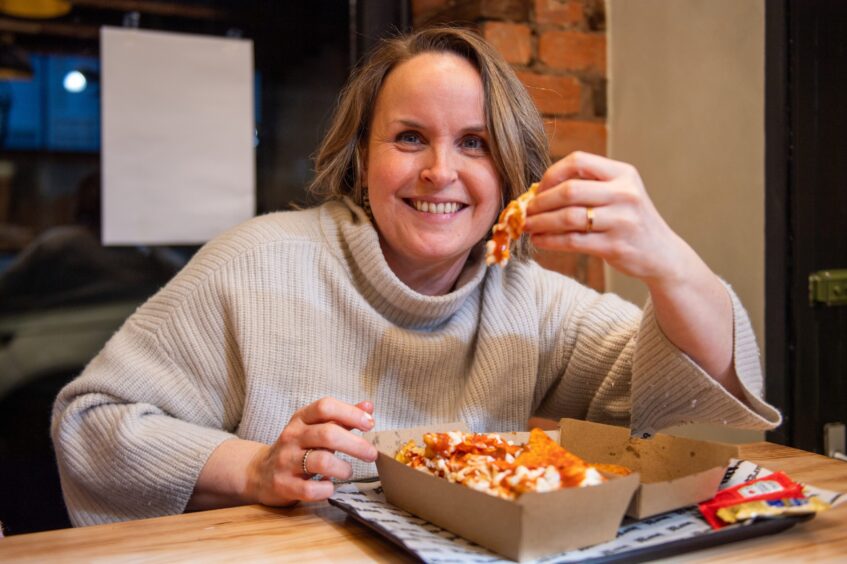 Rachel holds up a cheesy fry while smiling at the camera in Burgg.