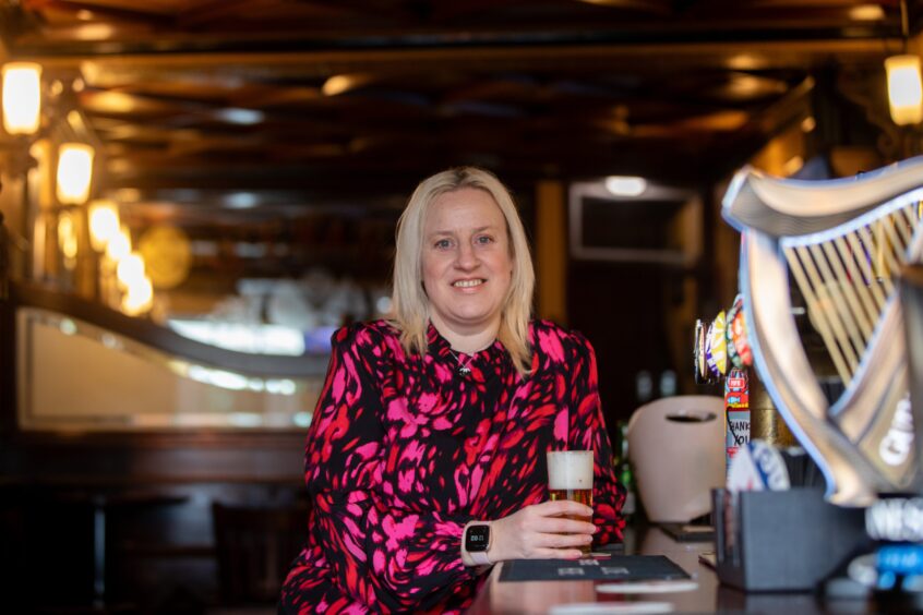 Debbie leans against the bar at the oldest pub in Dunfermline - The Old Inn