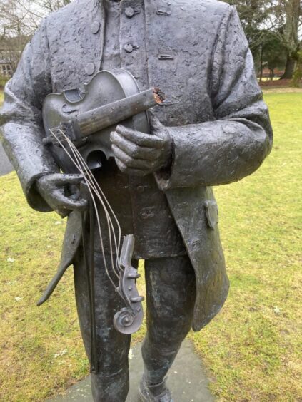 Close up of bronze Niel Gow statue with damaged fiddle