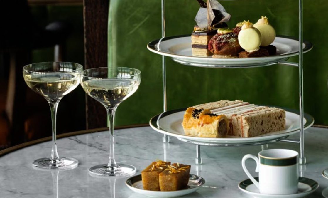 A selection of dainty sandwiches and pastries displayed on a cake stand with two coupes of champagne and two tea cups, which comes with afternoon tea at The Rusacks Hotel, St Andrews.