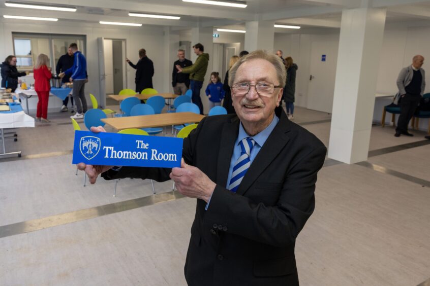 Sandy Thomson at pavilion, holding plaque which reads 'The Thomson Room' in front of group of people touring facilities