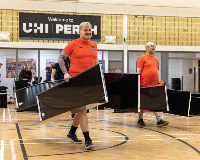 Two men walking onto sports court carrying pieces for new rink