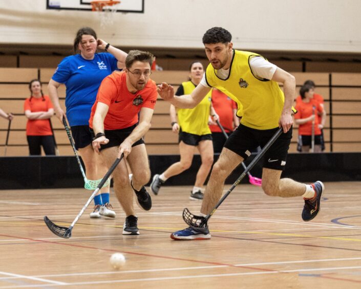 Small group of people playing floorball with sticks and small indoors ball