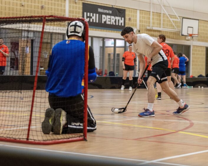 Person with floorball stick about the take aim at kneeling goalkeeper