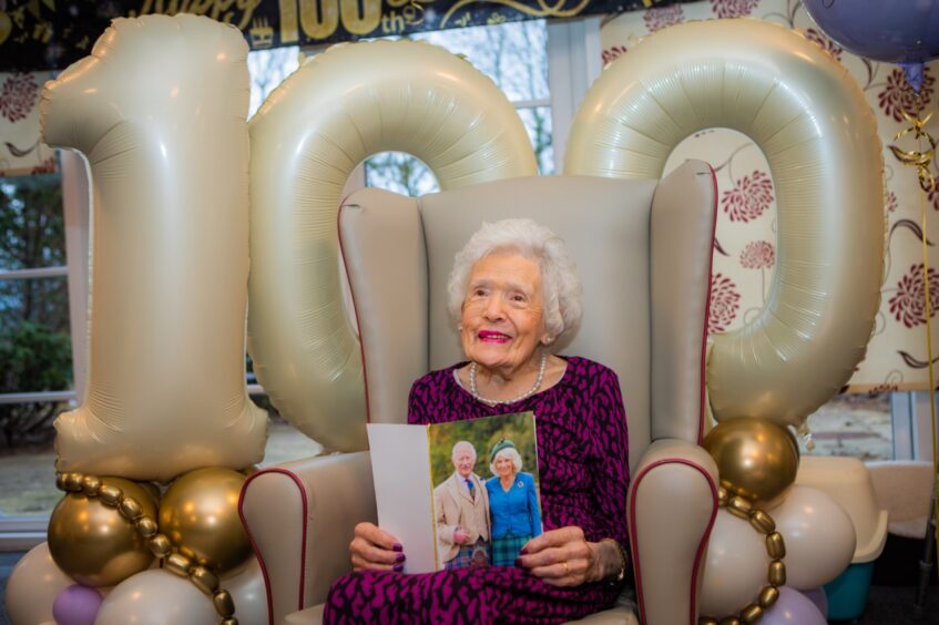 Betty Black seated with telegram from King and Queen in front of 100th birthday balloons