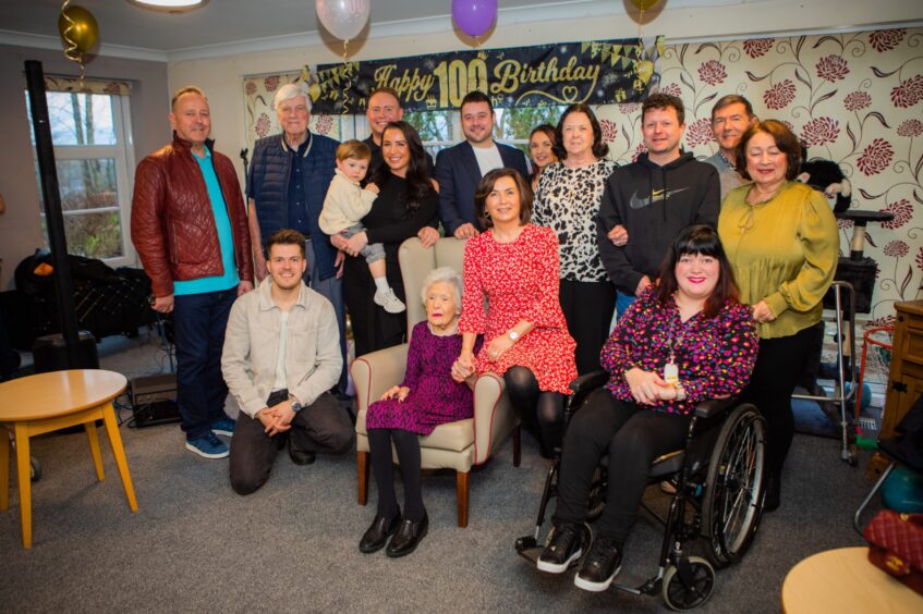 Betty Black, seated, surrounded by family members and 100th birthday banners and balloons