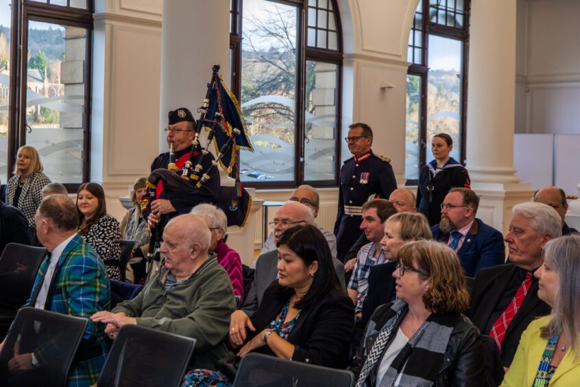 Group of people seated in Civic Hall as piper walks into room