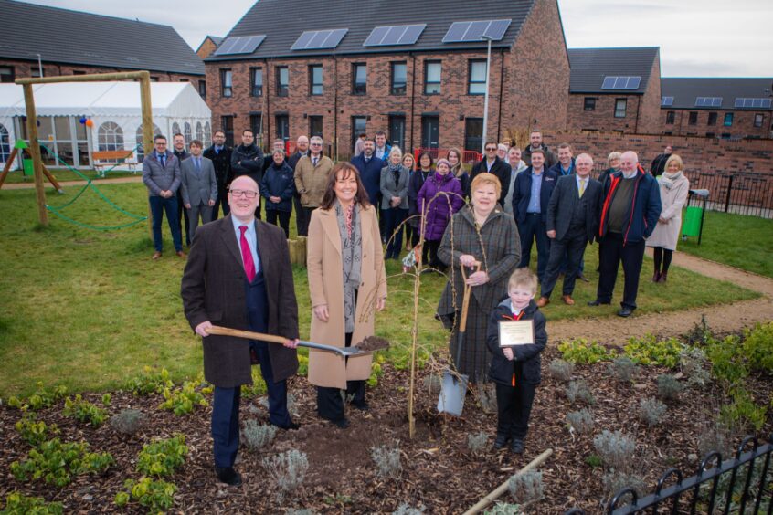 Kevin Stewart MSP planting tree in front of large group of people and new two storey housing on modern-day Muirton estate, Perth