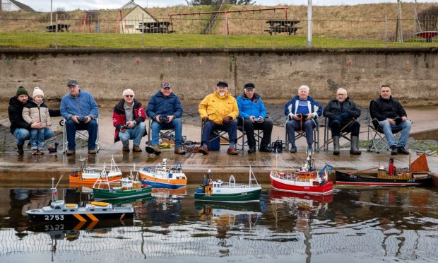 Image shows: Members of the Scottish Fisheries Museum sitting in directors' chairs at Cellardyke Tidal Pool ready for the morning's sailing. The men are sitting in a row with their model boats in the water in front of them.