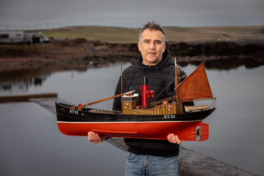 Image shows: Neil Thomson with a model of the boat his grandfather sailed in. Ian is standing by the water in Cellarydyke holding a large model boat with a red and black hull.