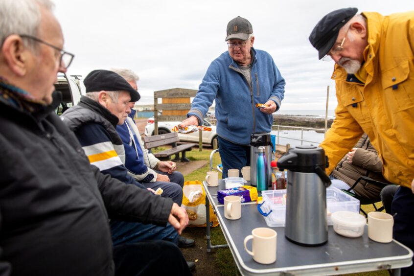 Image shows: a group of men warming up with a cup of tea after sailing their model boats at Cellardyke Tidal Pool.