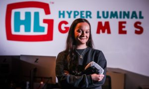 Video game tester Hannah in front of Hyper Luminal sign.