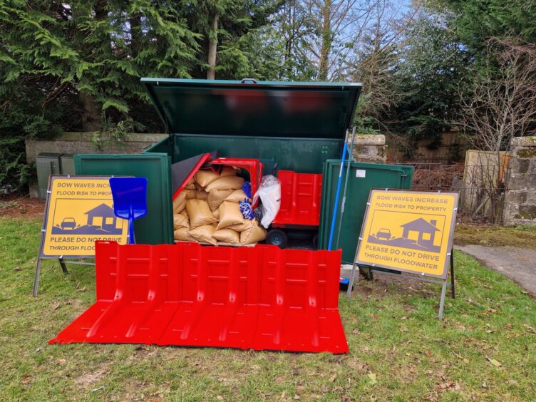 Metal container filled with sandbags with signs and flood protection equipment in front