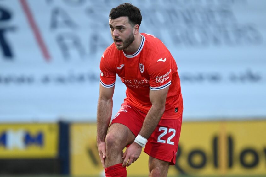 Jordan Doherty, wearing Raith Rovers' red third kit, reaches down to his sock.