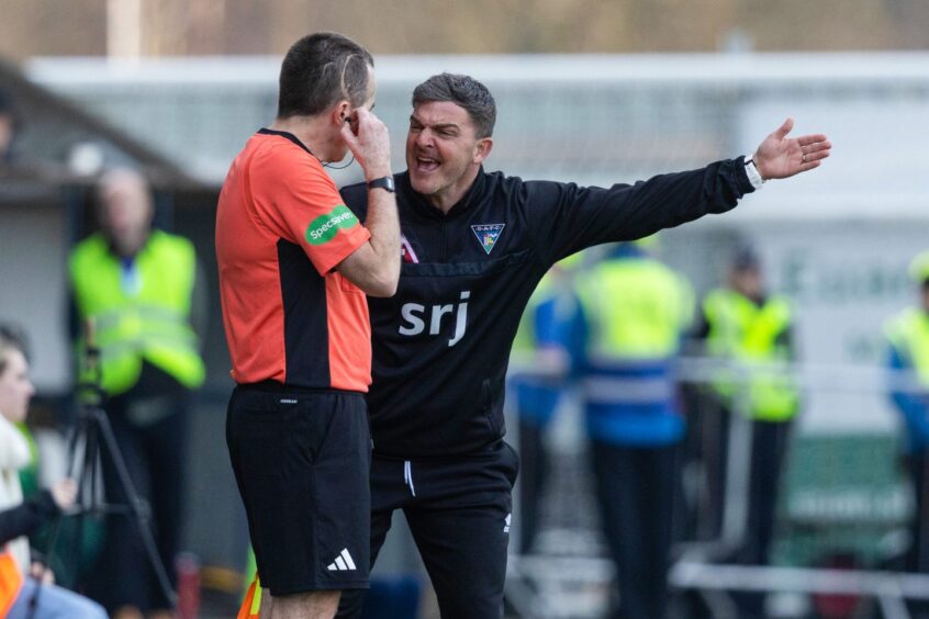 Kevin McDonald gesticulates with his left arm as he speaks animatedly to an assistant referee.