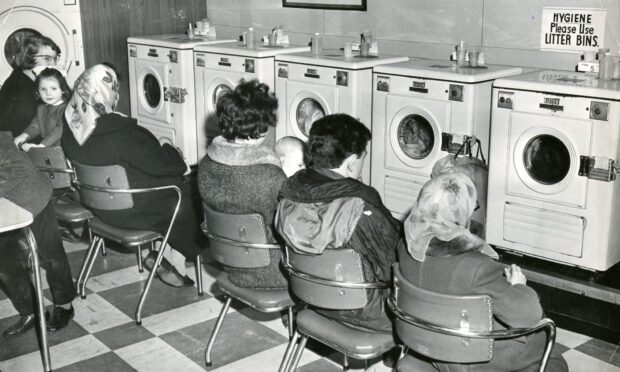 a row of women sit on chairs in front of machines at a self-service launderette in Lochee, Dundee