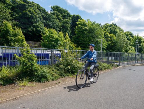 woman cycles on a tree-lined path as part of active travel in Fife