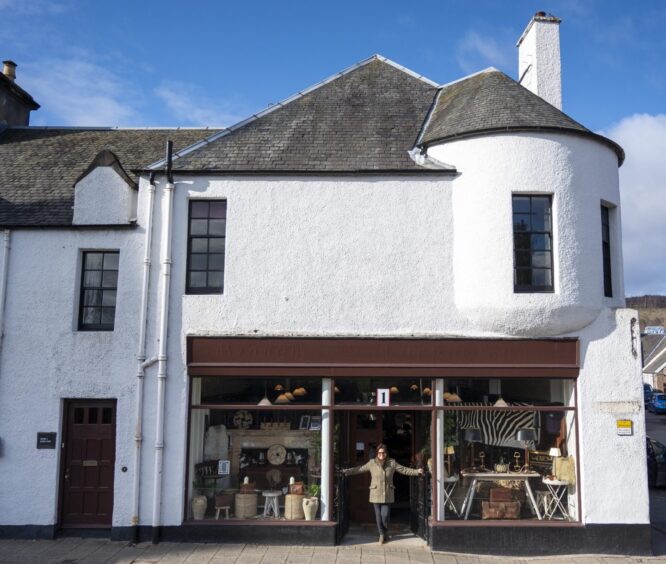 Elaine McConnochie standing at door to shop on ground floor of whitewashed two-storey building with turret