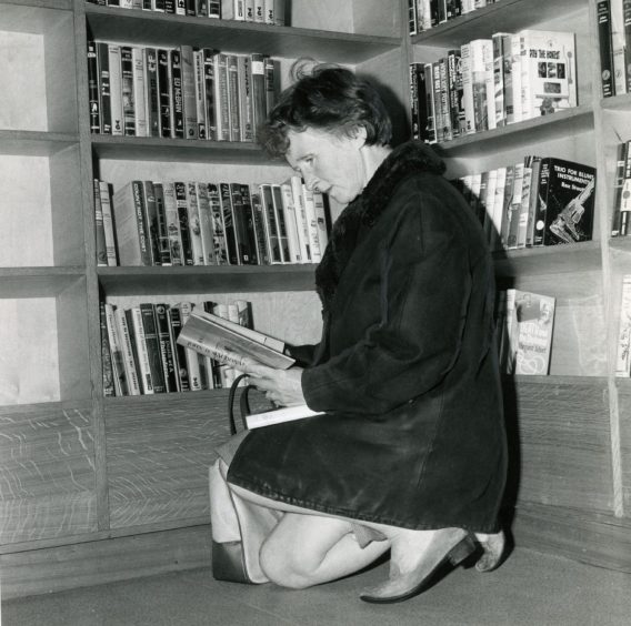 a kneeling woman browsing through the book selection at Douglas Library.