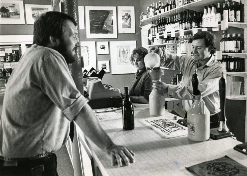 a man pours beer into a jug while another waits on the other side of a counter