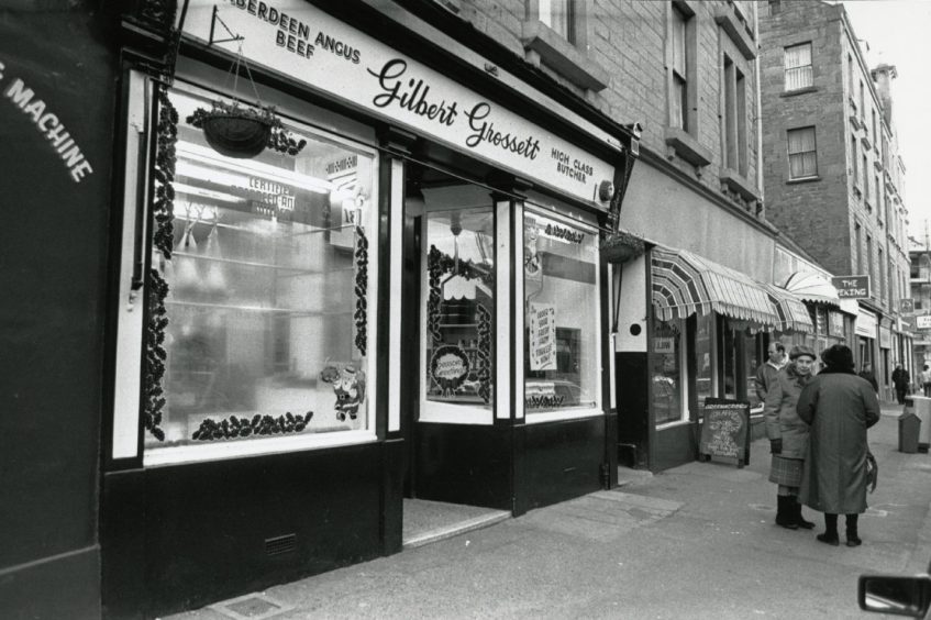 Pedestrians on the pavement outside the butcher's shop.