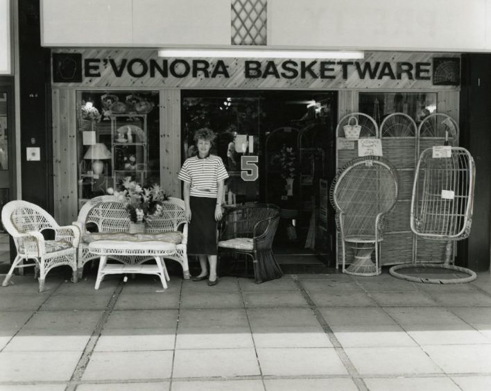 a woman stands beside a table and chairs outside the front of E'vonora Basketwear in June 1989.