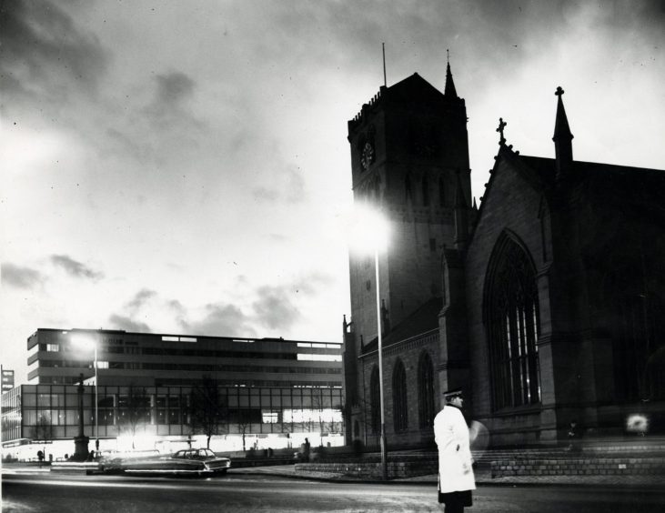 A policeman wearing a reflective coat is in the foreground, looking west towards the Steeple Church and the Angus Hotel in November 1965.