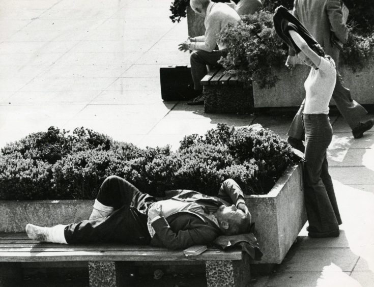 People sit and catch the sun on benches outside Dundee's Overgate