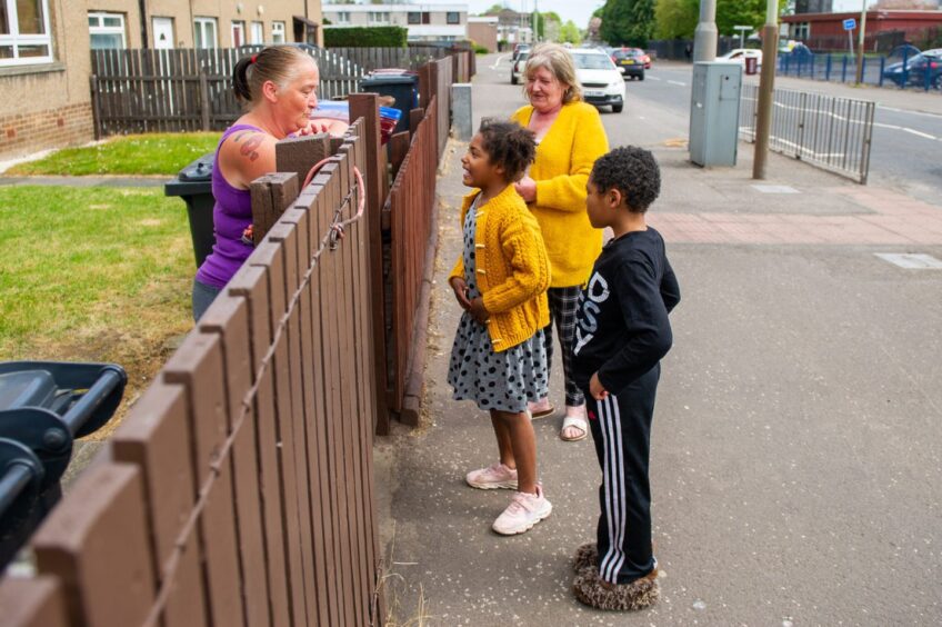 Two adults and two children on either side of a garden fence have a socially distanced chat in Dundee's Happyhillock Road. 