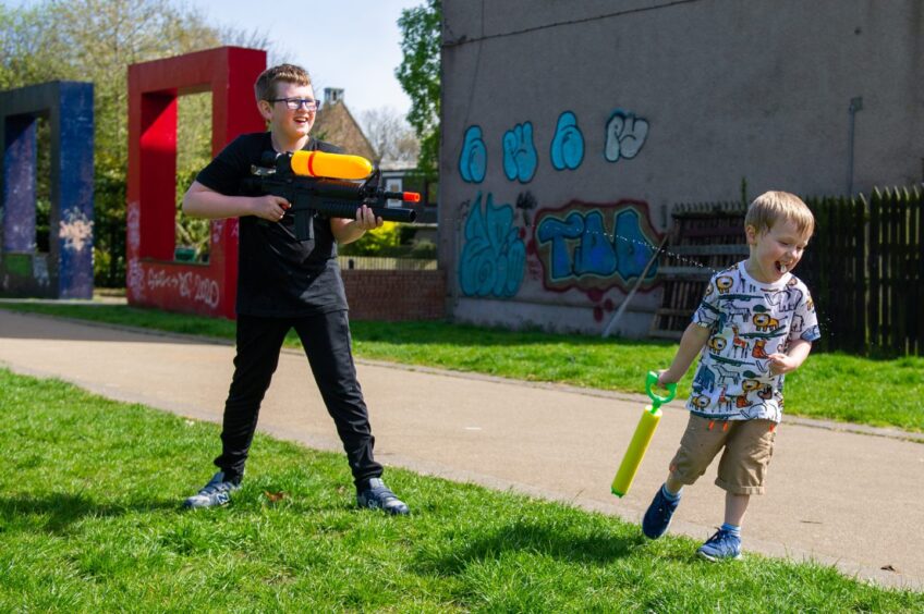 two children have fun with waterguns in Dundee's Hilltown during daily exercise. 